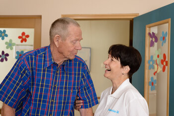 Eine Pflegerin und ein älterer Mann lachen.